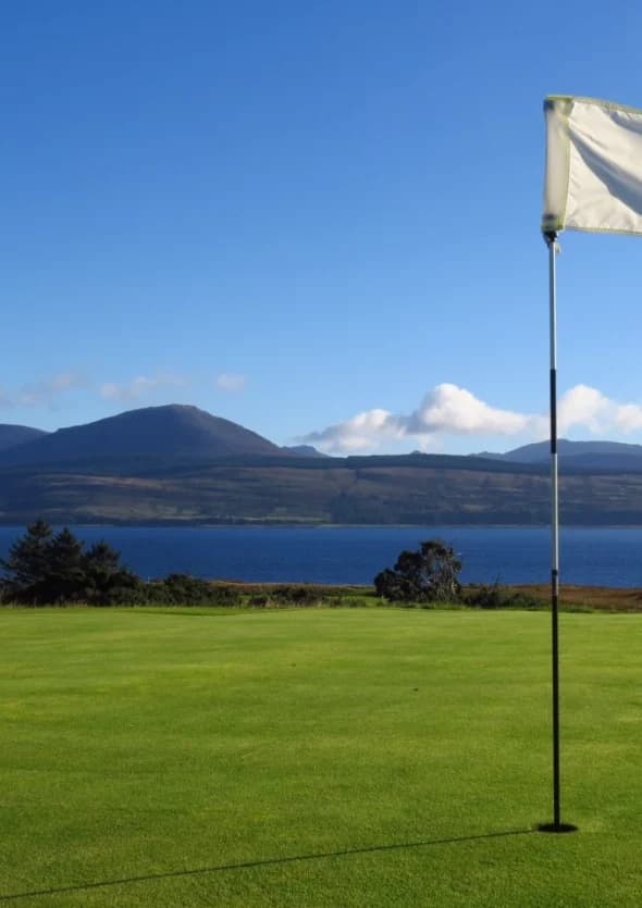 A flag on a Carradale Golf Club green with views across the water to Arran